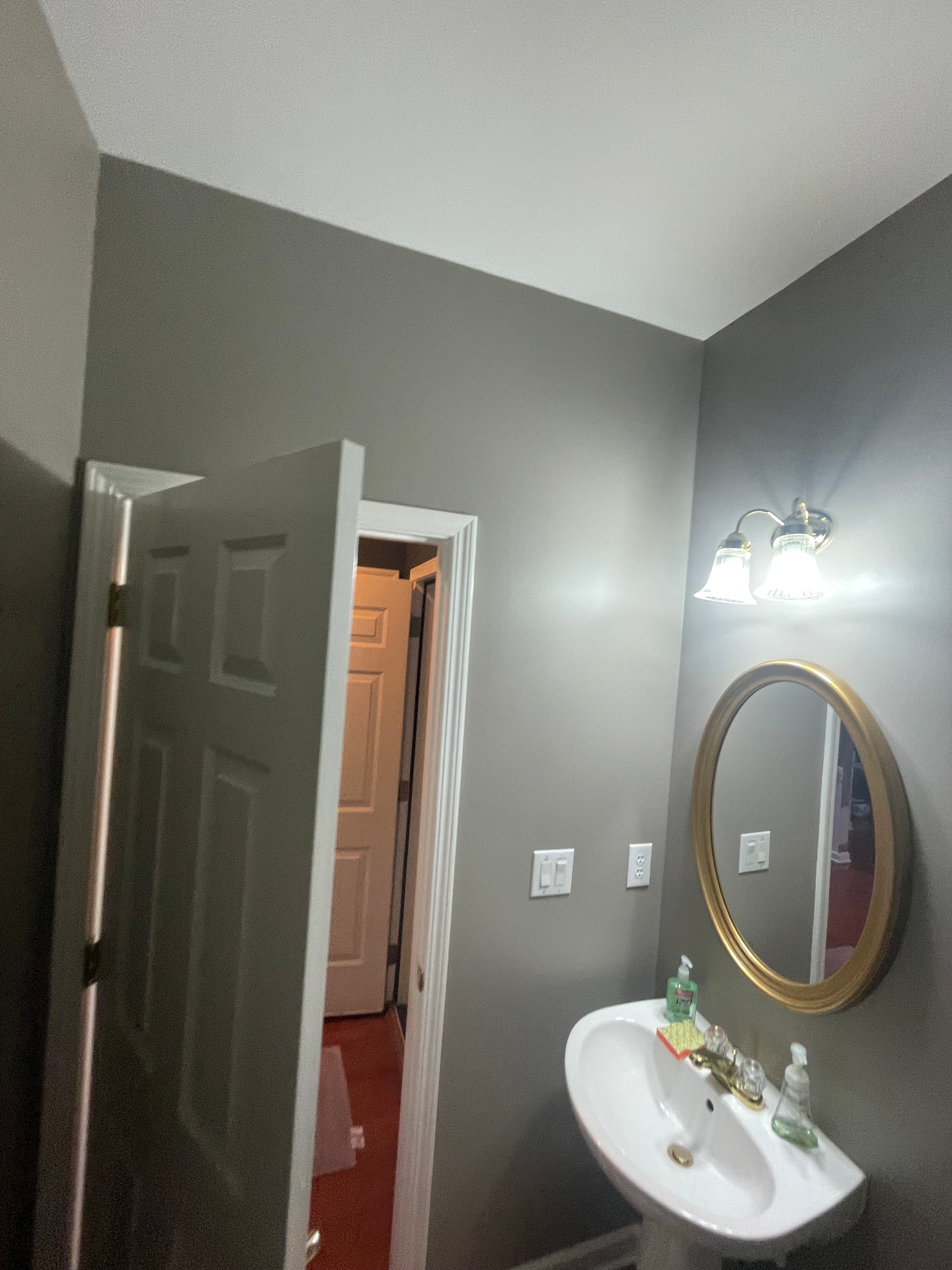 Powder room with gray walls, white trim, and a gold-framed mirror over a pedestal sink